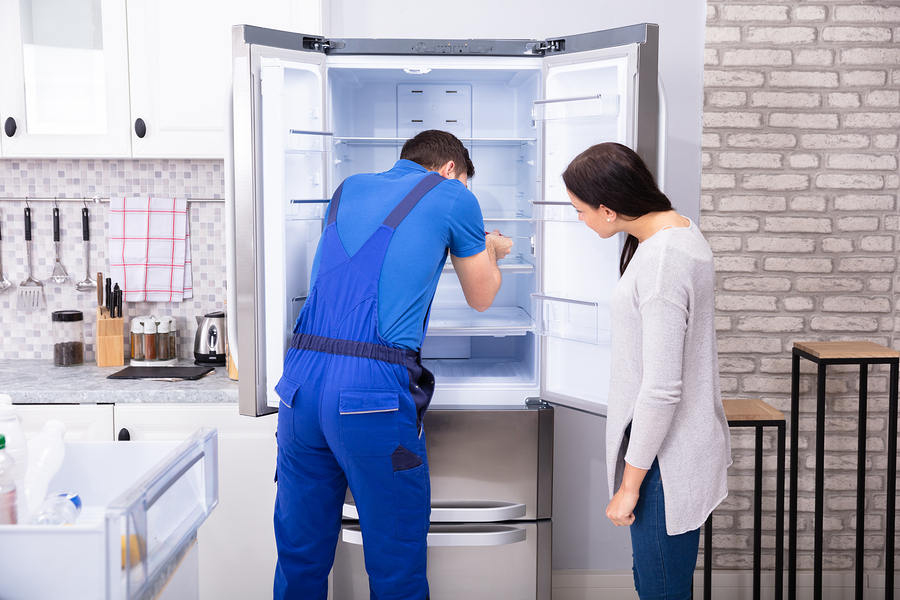 Woman Looking At Male Repairman Fixing Refrigerator With Screwdr